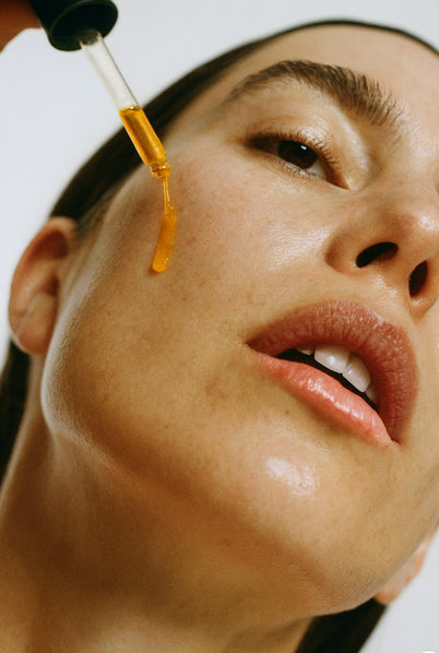 Close-up of a person applying a dropper of liquid to their face.