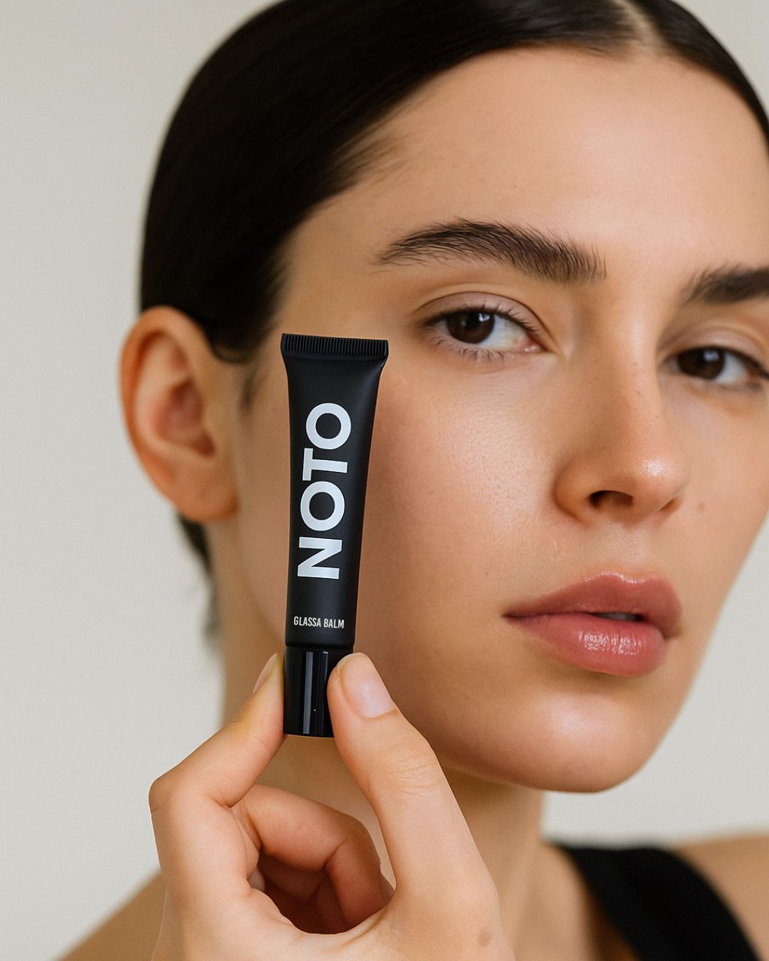 Woman holding a black tube labeled 'Noto' against her face.