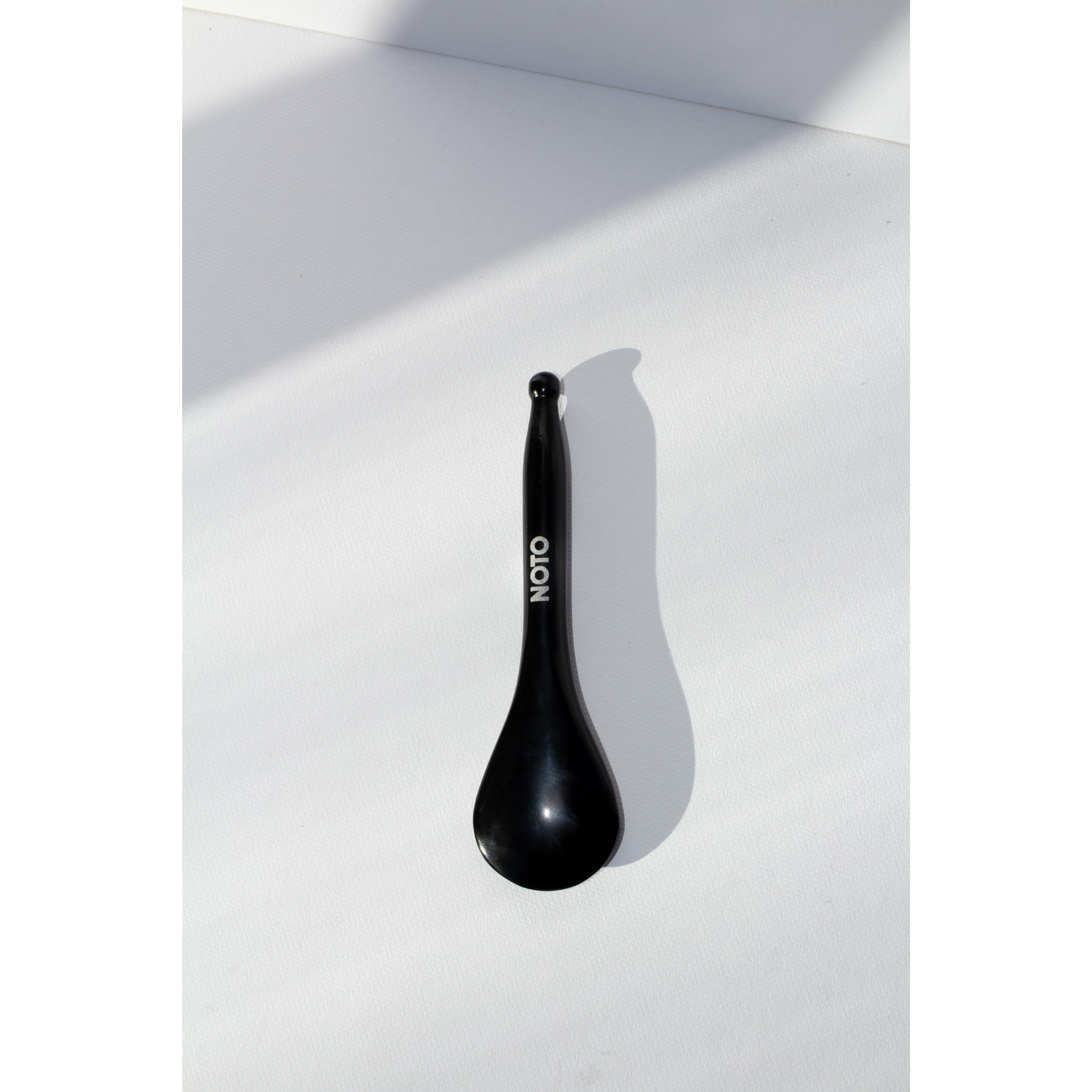 A black Bian stone Gua Sha facial tool lying on a white surface.